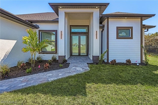 view of exterior entry featuring a yard, french doors, and stucco siding