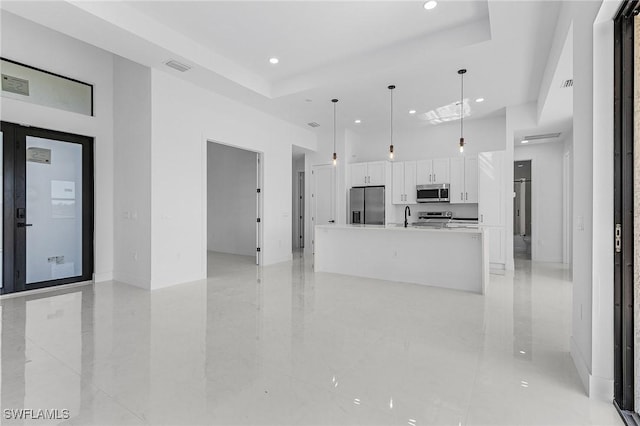 kitchen featuring visible vents, white cabinetry, stainless steel appliances, a large island with sink, and hanging light fixtures