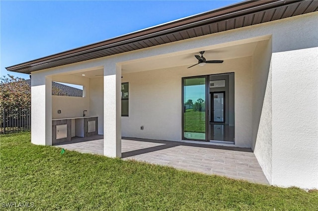 rear view of property featuring a yard, stucco siding, an outdoor kitchen, and a patio