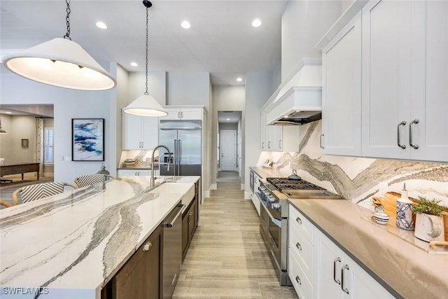 kitchen featuring premium range hood, decorative light fixtures, high quality appliances, a large island, and white cabinets