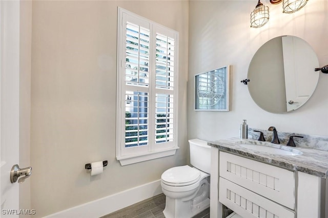 half bath featuring toilet, vanity, baseboards, and wood finished floors