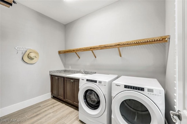 washroom featuring light wood-type flooring, a sink, cabinet space, baseboards, and washing machine and clothes dryer