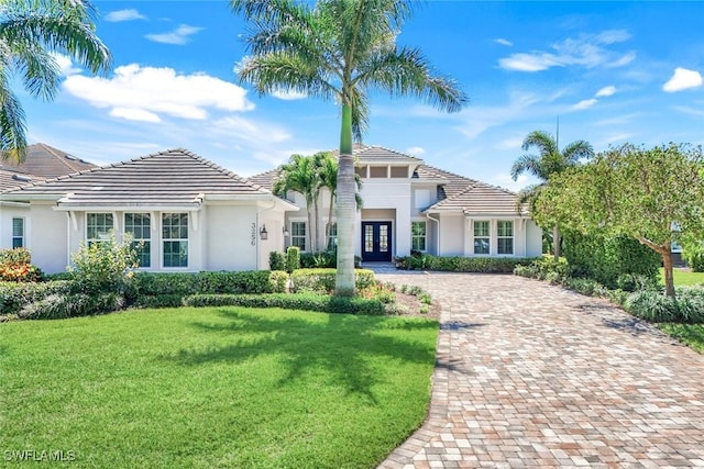 mediterranean / spanish home with a front yard, stucco siding, french doors, a tile roof, and decorative driveway