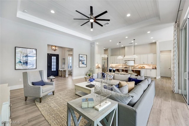 living room featuring visible vents, a ceiling fan, light wood-style floors, and a tray ceiling