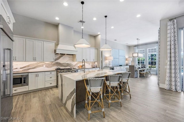 kitchen with premium range hood, a sink, white cabinets, stainless steel microwave, and backsplash