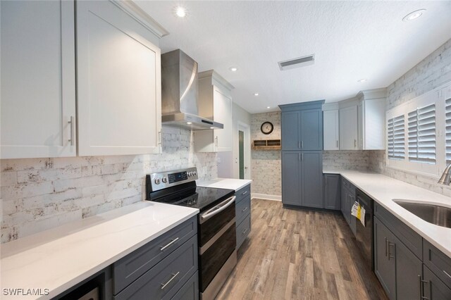 kitchen featuring double oven range, light countertops, black dishwasher, wall chimney exhaust hood, and a sink