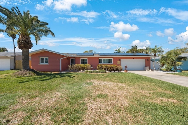 ranch-style house with roof mounted solar panels, concrete driveway, a front lawn, and a garage