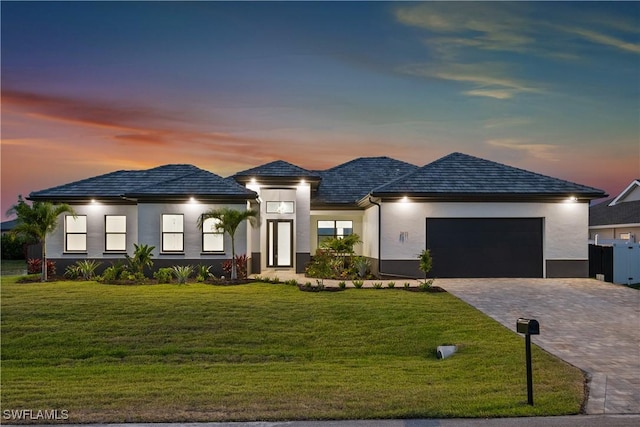 prairie-style house featuring decorative driveway, a front lawn, an attached garage, and stucco siding