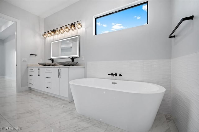 bathroom with a sink, double vanity, marble finish floor, and a freestanding bath