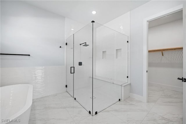 full bath featuring a freestanding tub, a spacious closet, marble finish floor, and a shower stall