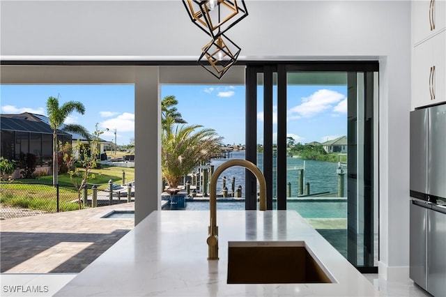 kitchen with a water view, decorative light fixtures, freestanding refrigerator, white cabinets, and a sink