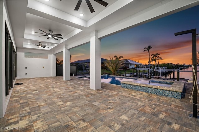 patio terrace at dusk with an outdoor pool, an in ground hot tub, a boat dock, and a ceiling fan