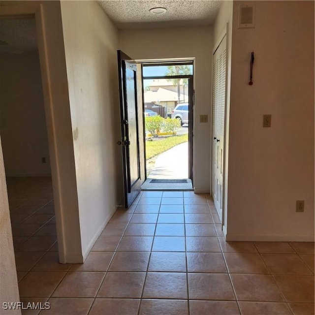 doorway to outside with light tile patterned floors, baseboards, visible vents, and a textured ceiling