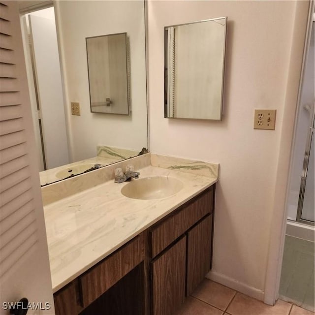 full bath featuring tile patterned flooring, vanity, baseboards, and a shower with door