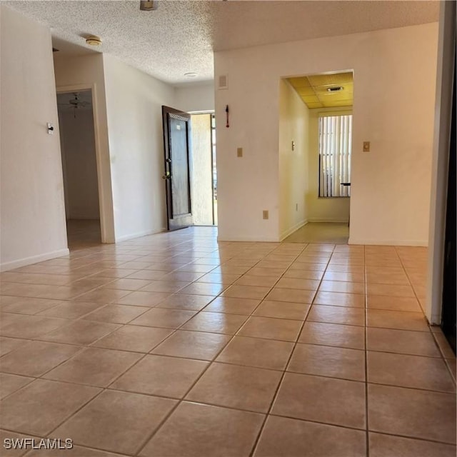 spare room featuring light tile patterned floors, baseboards, and a textured ceiling