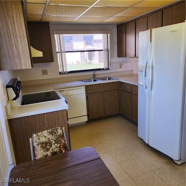 kitchen with white appliances, light floors, a drop ceiling, a sink, and light countertops