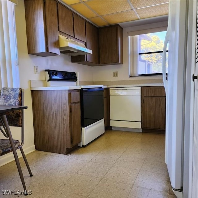 kitchen featuring white appliances, light floors, a drop ceiling, light countertops, and under cabinet range hood