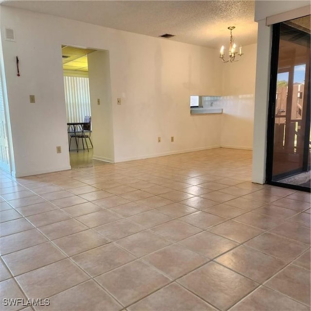 spare room featuring baseboards, visible vents, light tile patterned flooring, a textured ceiling, and a notable chandelier