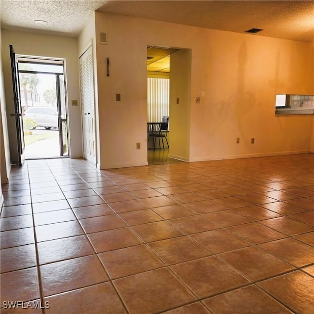 tiled spare room featuring visible vents, a textured ceiling, and baseboards