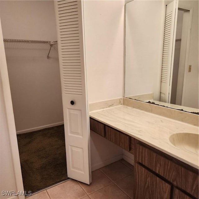 bathroom featuring tile patterned floors, vanity, a walk in closet, and baseboards