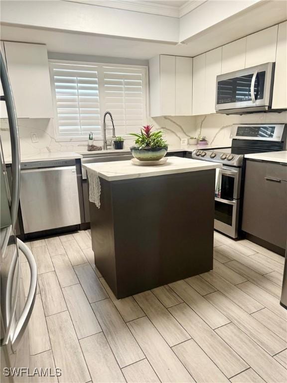 kitchen featuring a kitchen island, white cabinetry, appliances with stainless steel finishes, light countertops, and decorative backsplash