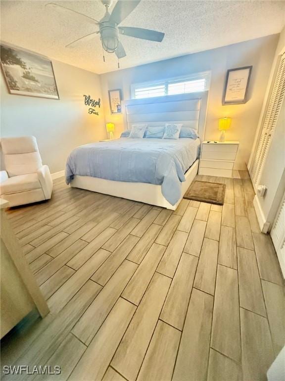 bedroom featuring a ceiling fan, baseboards, a textured ceiling, and wood tiled floor