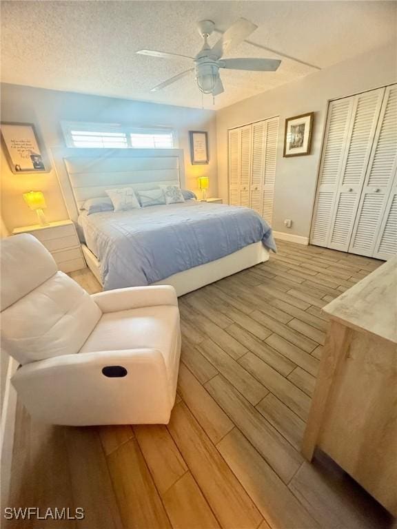 bedroom featuring two closets, a textured ceiling, wood finished floors, baseboards, and ceiling fan