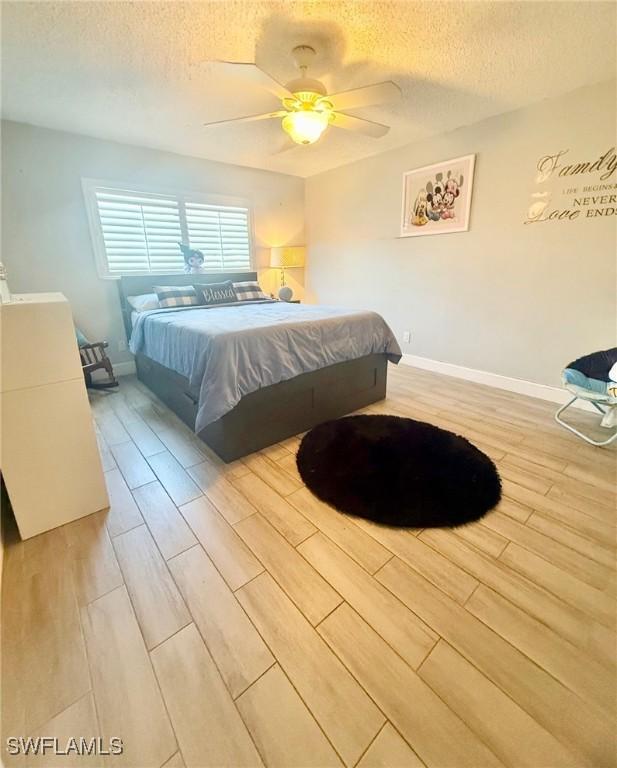 bedroom with a textured ceiling, a ceiling fan, baseboards, and wood finished floors