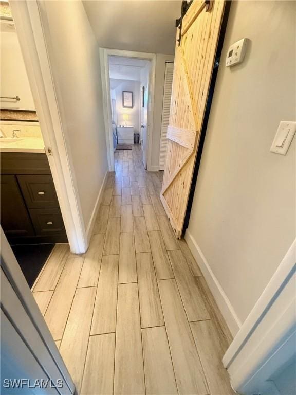 hallway with a barn door, baseboards, and wood finish floors