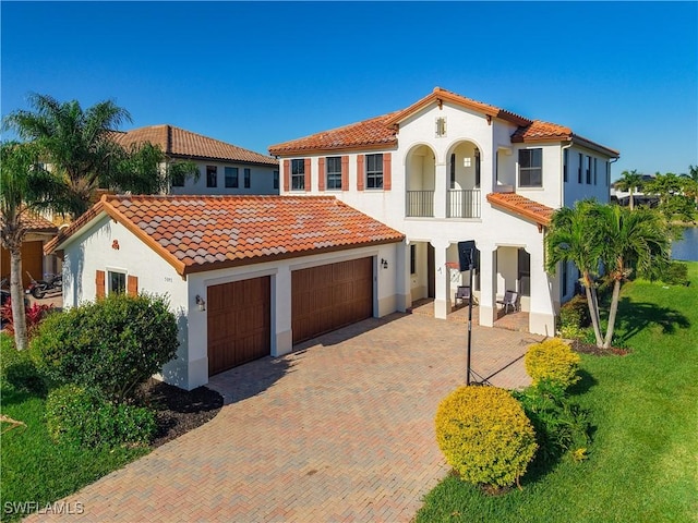 mediterranean / spanish house featuring decorative driveway, a front lawn, stucco siding, and a tiled roof