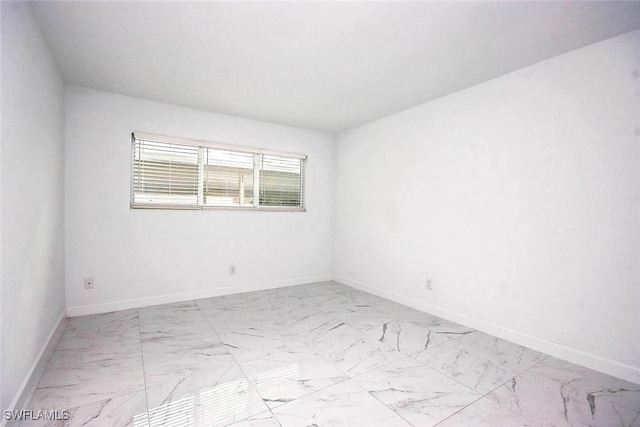 unfurnished room featuring marble finish floor and baseboards