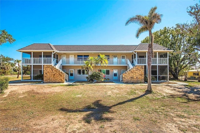 rear view of property featuring stucco siding, a tiled roof, stairs, and a yard