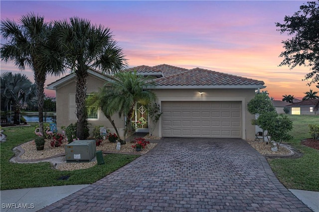 ranch-style home featuring a tiled roof, stucco siding, a lawn, decorative driveway, and a garage