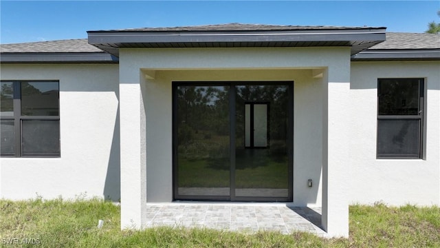 entrance to property featuring stucco siding and a shingled roof