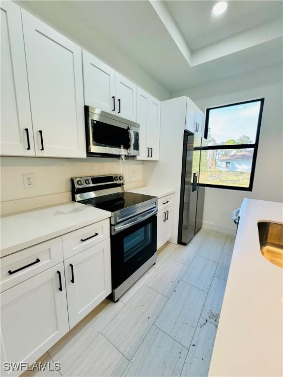 kitchen featuring white cabinets, stainless steel appliances, light countertops, and baseboards