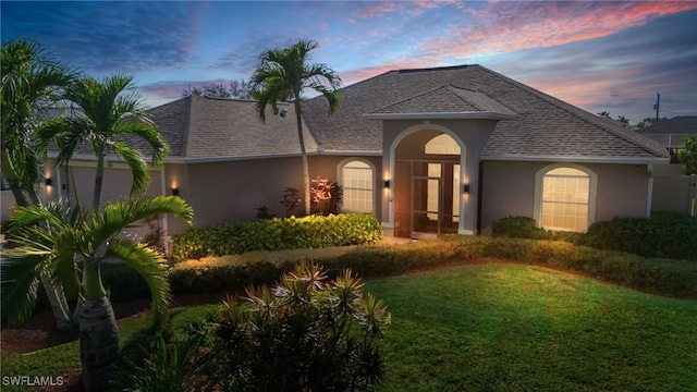 view of front facade with a shingled roof, a lawn, and stucco siding