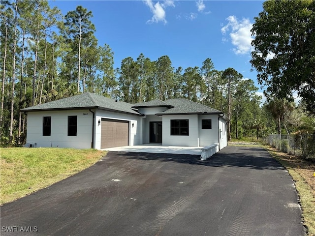 view of front of house with aphalt driveway, fence, a garage, and roof with shingles