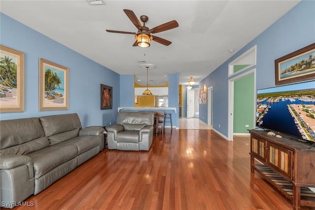 living area featuring visible vents, baseboards, a ceiling fan, and wood finished floors