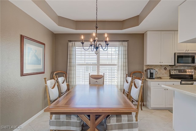 dining space with light tile patterned floors, a tray ceiling, baseboards, and a notable chandelier