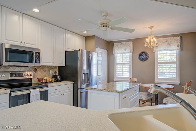 kitchen with backsplash, ceiling fan with notable chandelier, stainless steel appliances, white cabinetry, and a sink