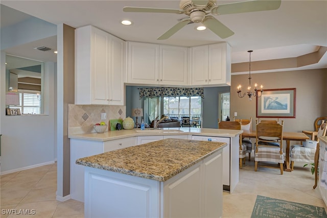 kitchen with a sink, tasteful backsplash, white cabinetry, a peninsula, and a healthy amount of sunlight