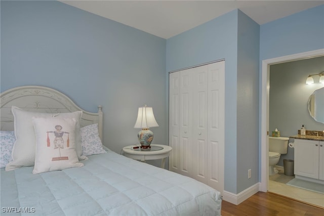 bedroom with connected bathroom, wood finished floors, a closet, and baseboards