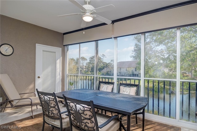 sunroom with a ceiling fan and a water view