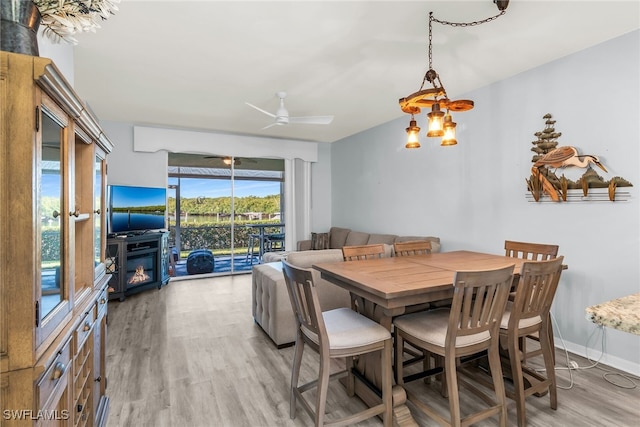 dining area featuring a glass covered fireplace, baseboards, light wood-type flooring, and a ceiling fan