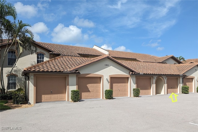 mediterranean / spanish house with community garages, a tile roof, and stucco siding