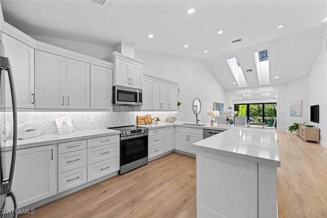 kitchen featuring a peninsula, a skylight, a sink, white cabinets, and appliances with stainless steel finishes