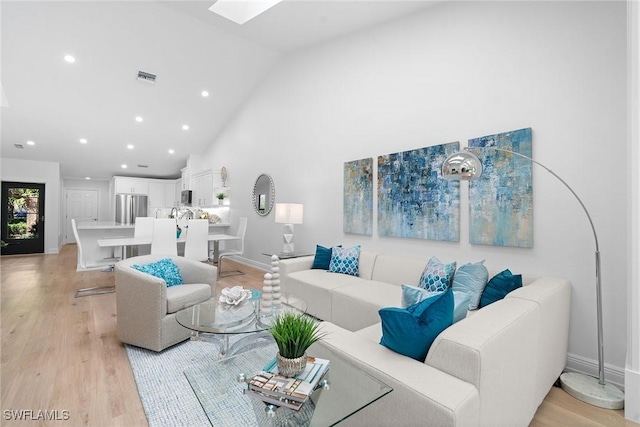 living room with baseboards, visible vents, light wood finished floors, high vaulted ceiling, and a skylight