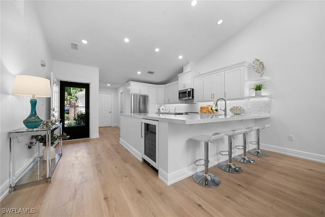 kitchen featuring beverage cooler, white cabinetry, a peninsula, appliances with stainless steel finishes, and light wood finished floors