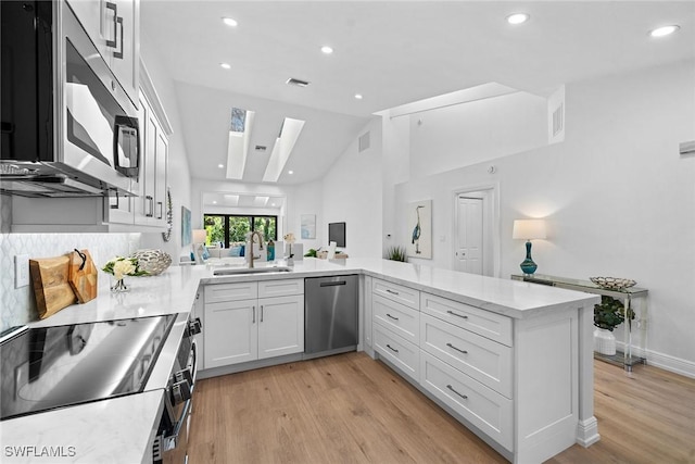 kitchen featuring visible vents, a sink, stainless steel appliances, light wood-style floors, and a peninsula