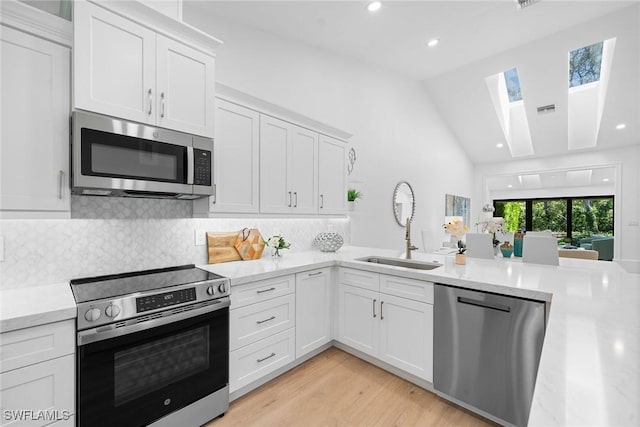 kitchen featuring visible vents, a sink, appliances with stainless steel finishes, white cabinetry, and lofted ceiling with skylight